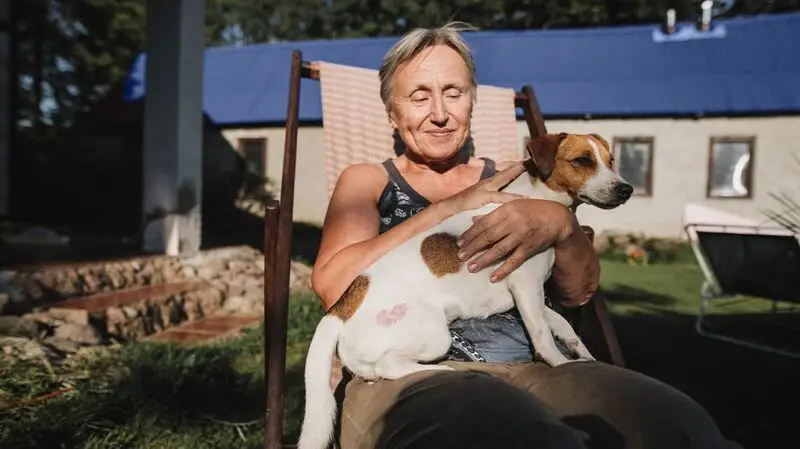 An older adult woman hold a dog in her arms while sitting on a chair outside