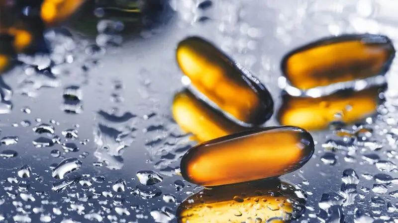 Omega-3 capsules, which are polyunsaturated fatty acids, sit on a wet reflective surface