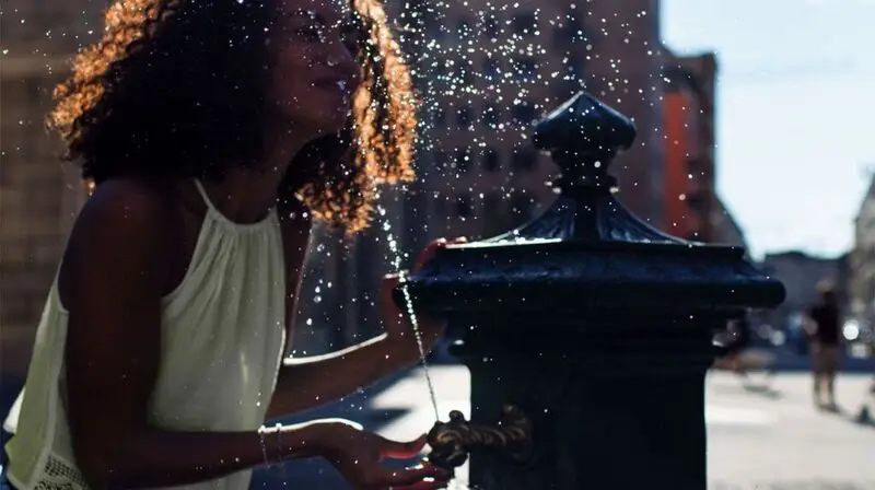 young Black woman splashing her face with water from a public water fountain