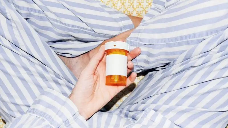 hand holding orange pill box of prescription medicine