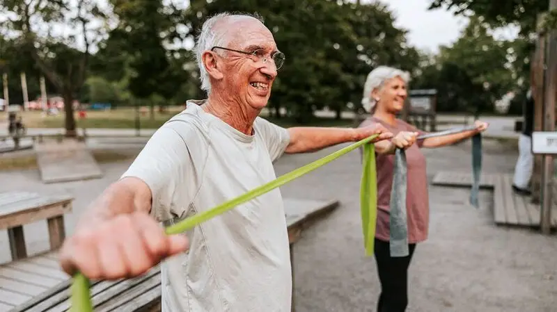 Two older adults doing arm band stretching exercises outside in a park