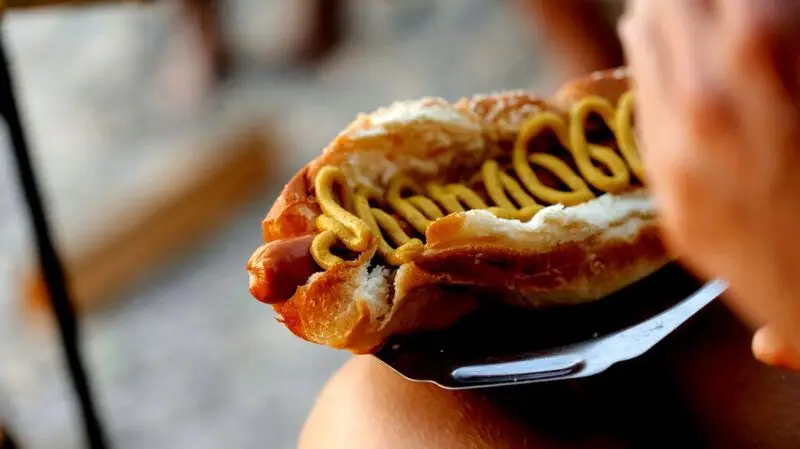 A person holding a hot dog with mustard, a type of ultraprocessed food