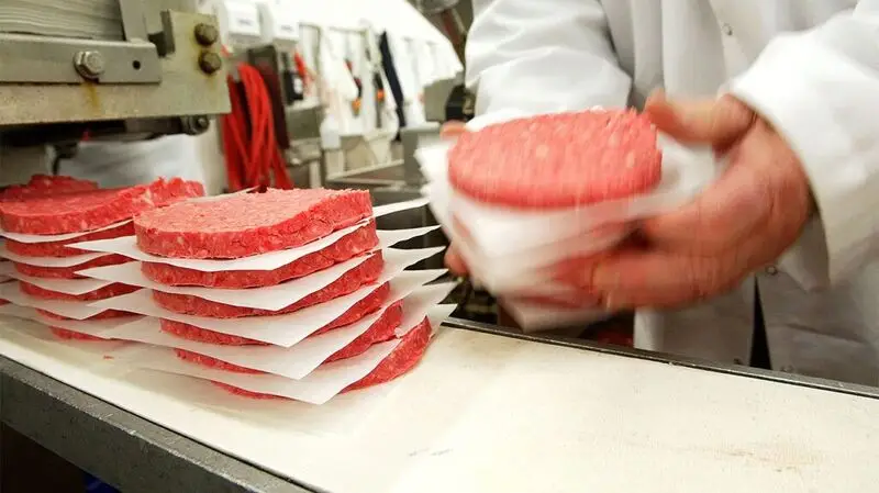 A person stacking up uncooked hamburger patties, which are considered inflammatory foods, in between sheets of parchment paper on a kitchen worktop