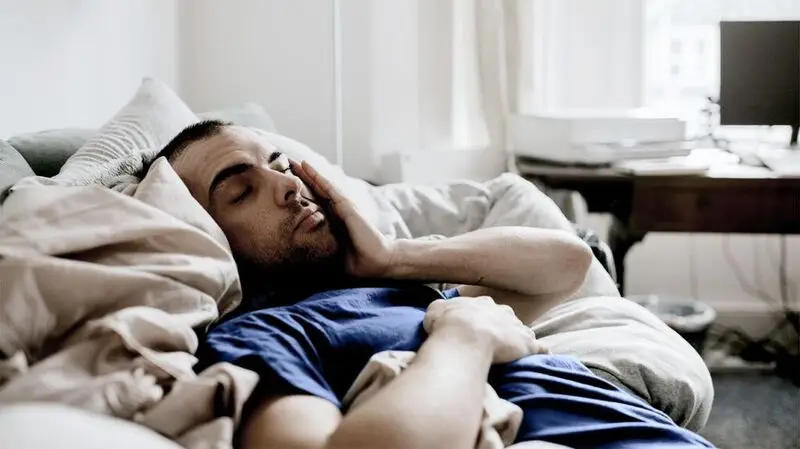 A tired man sleeping in a bed, holding his face with one of his hands