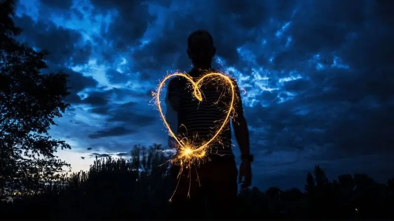 A long exposure photograph of a person drawing a heart with light at night