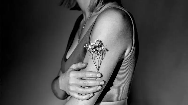 black and white photo of person holding small flowers up against their arm