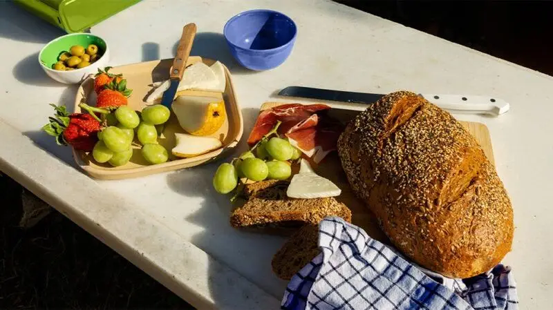 A plate full of cut fruit, cheese, and olives, accompanied by a loaf of wholegrain bread to showcase a Mediterranean style diet