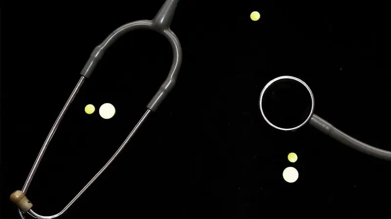 A stethoscope used to listen to the heart and a few beta blocker pills on a flat dark surface
