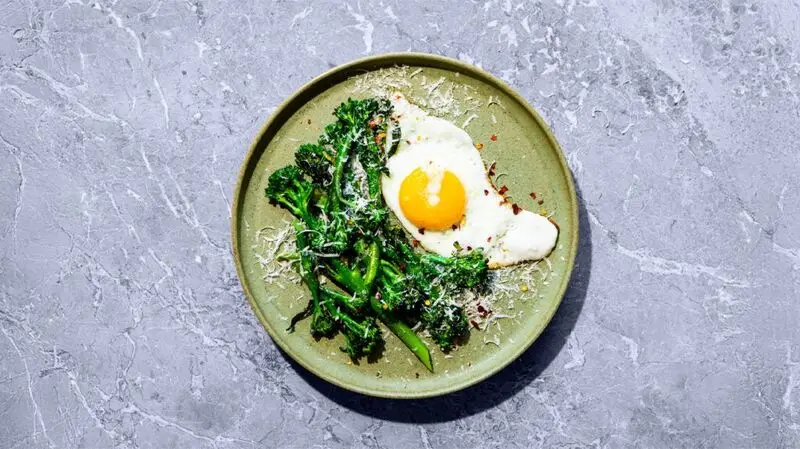 A plate of broccoli covered in parmesan and. a fried egg, an example of a keto-friendly diet.