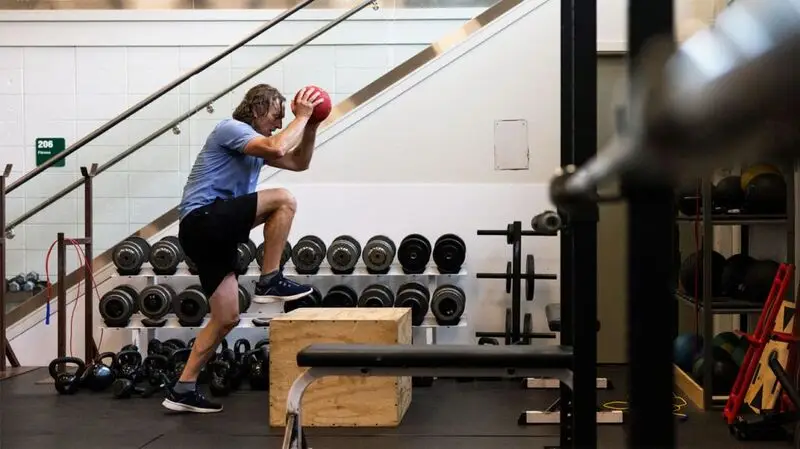 An older adult exercises with a medicine ball and box to step on in a gym