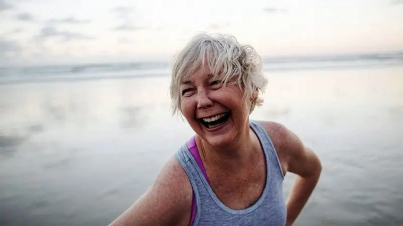 An older adult woman laughing, hands on the hips looking to the side