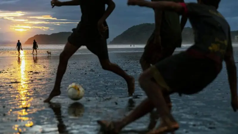young people playing football on the beach at sunset