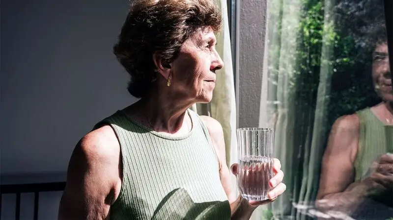 older white woman holding a glass of water and looking out the window