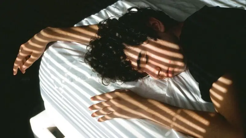 young white man with curly black hair asleep on bed