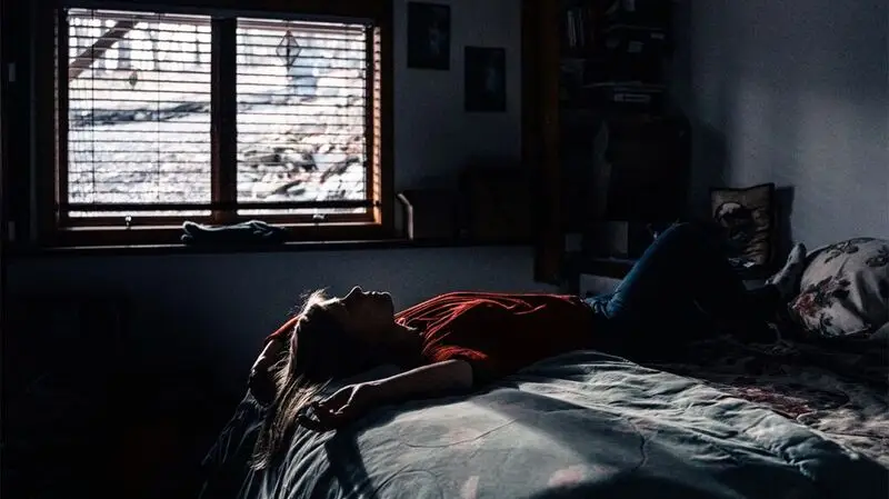 A person laying on bed as the sun pours in through the window.