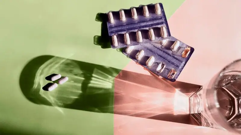 two blister packs of cholesterol lowering drugs against green and pink background