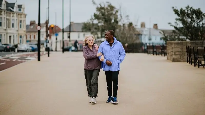 An older adult couple walking outside, linked arm in arm, smiling