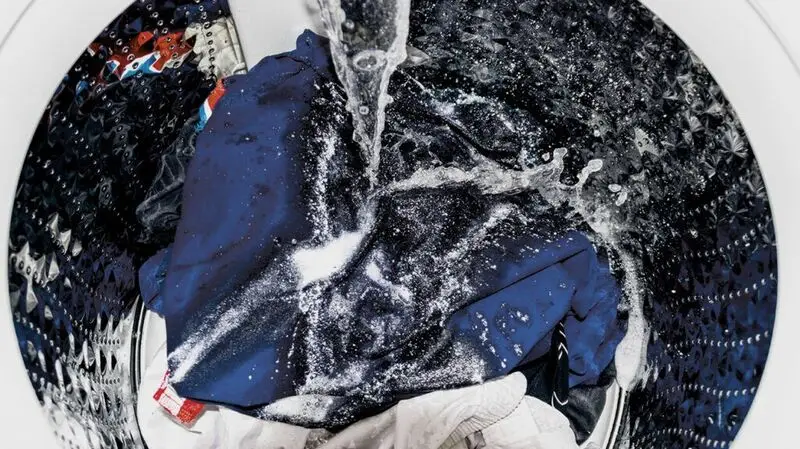 Clothing items being submerged in a perchloroethylene bath in a specialized machine.