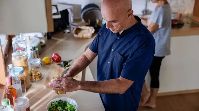 older bald man squeezing a lemon over an avocado salad