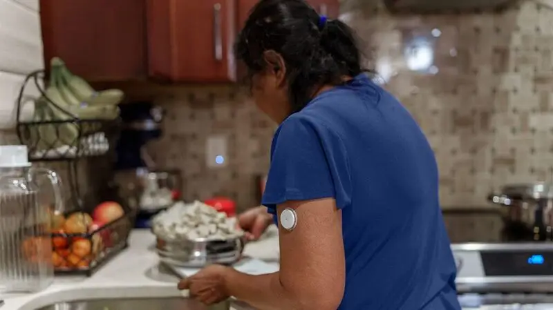 Indian woman with glucose monitor seen from the back in the kitchen