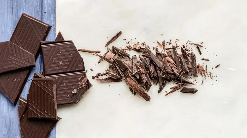 Broken and shredded pieces of a dark chocolate bar on a two-tone surface