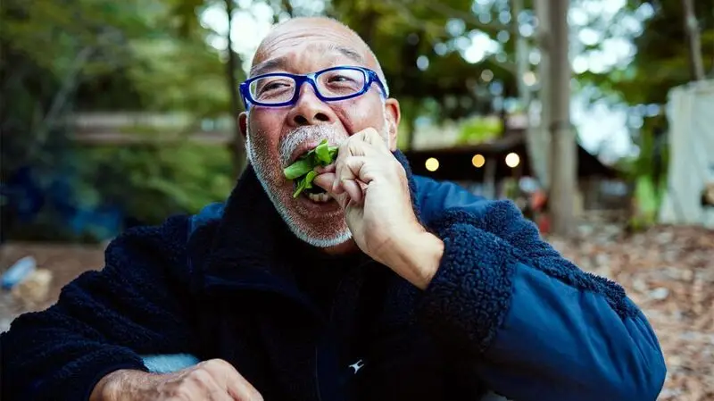 Older male sitting outside eating a salad with his hands