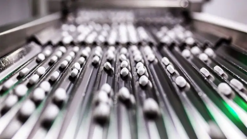 Rows of weight loss pills are on a conveyer belt in a pharmaceutical lab