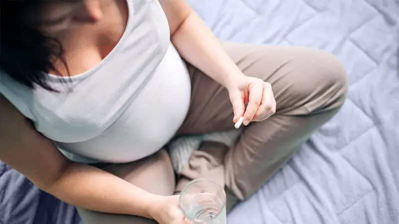 pregnant individual holding a pill and a glass of water