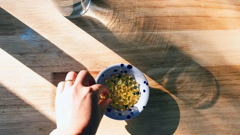 Vitamin D capsules in a partially sunlit bowl on a wooden table