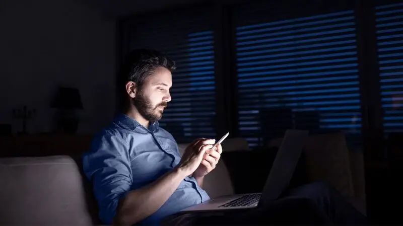 young man in blue dress shirt looking at his phone screen in the dark