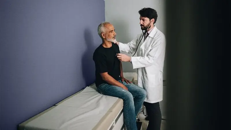 A doctor listens to a male patient's heart with a stethoscope