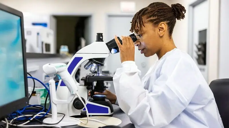 Black female researcher looking at sample through microscope