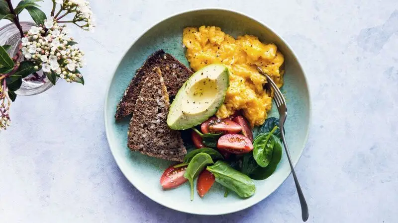 breakfast bowl of scrambled eggs, seeded bread, avocado, tomatoes, and spinach