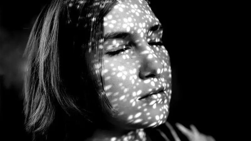 A person stands with their eyes closed, dots of light across their face