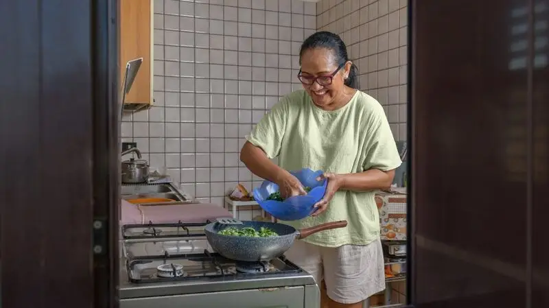 A woman prepares a healthy mail, cooking with various greens in a wok on a stove top in a kitchen