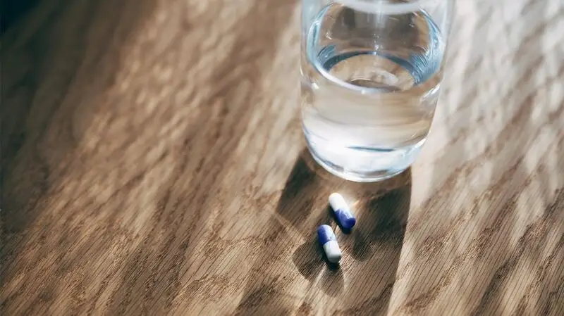 two aspirin pills by a glass of water on a wooden surface