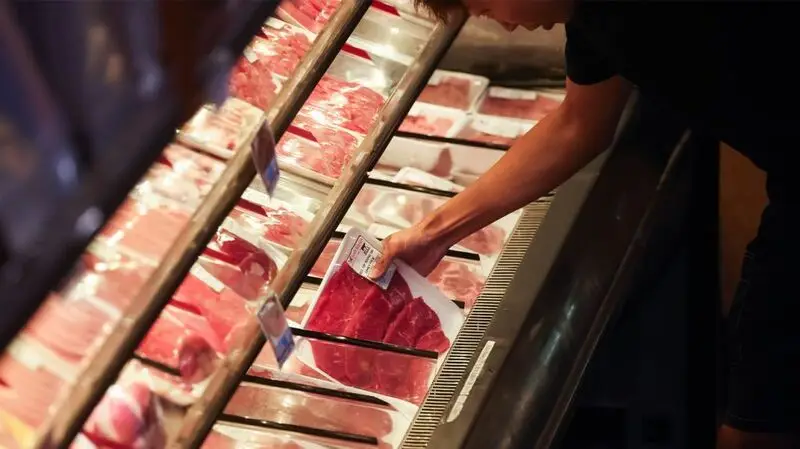 A person picking up a pack of red meat from a counter