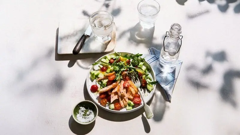 A plate of salmon salad, appropriate for a ketogenic diet with a bowl of salt and a bottle and glass of water next to it