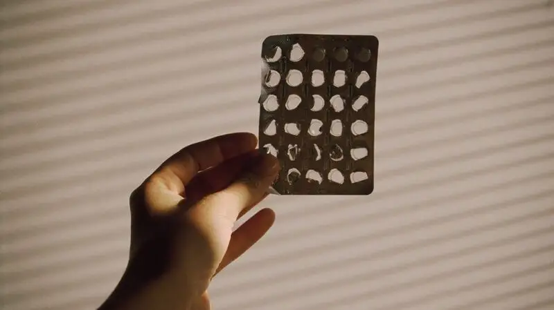 A person holds a blister pack of multivitamins in front of a wall as sunlight hits it