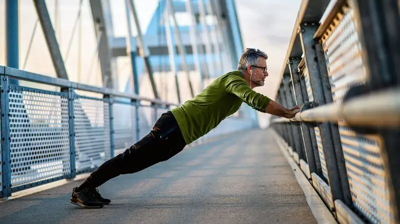 An older man does push ups against a railing