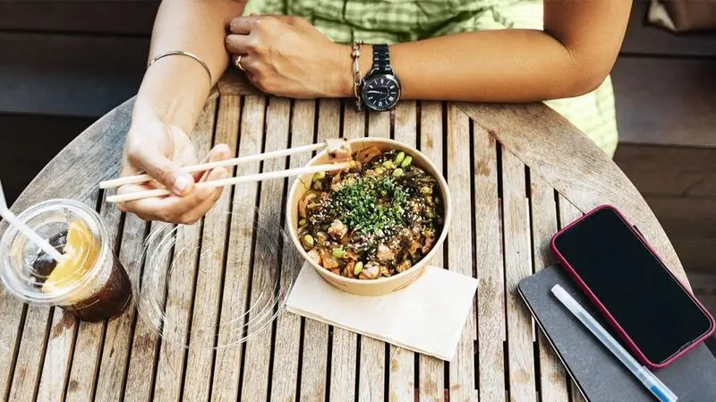 A person eating a healthy lunch outside using chopsticks.