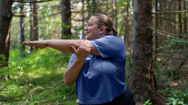 A woman with central obesity stretches her arms in the woods as part of her workout
