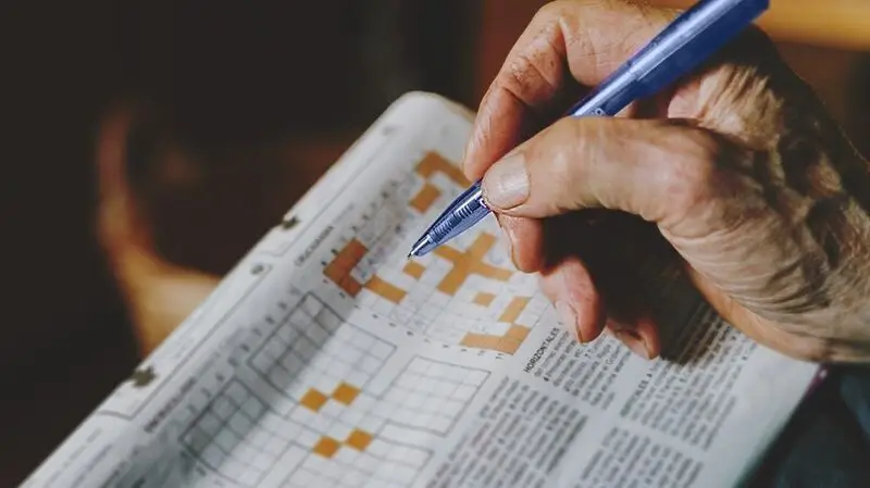 A person does a crossword puzzle on a newspaper