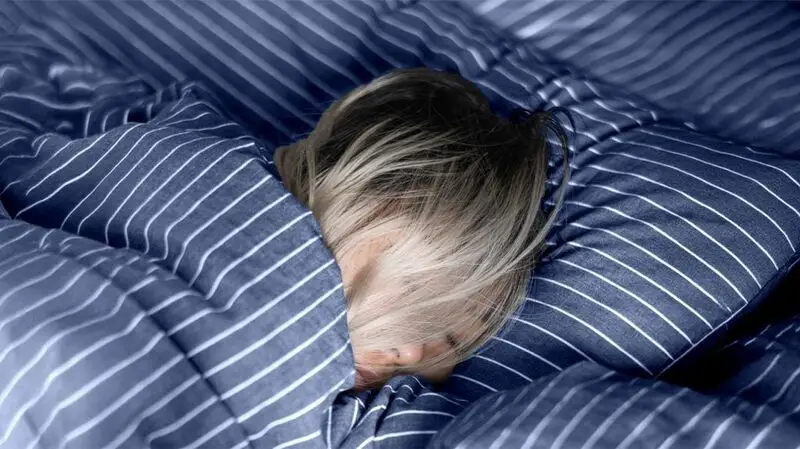 blond person asleep in bed with striped blue sheets