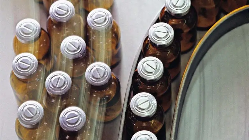 Vials of cholesterol-lowering medication lined up on a conveyer belt