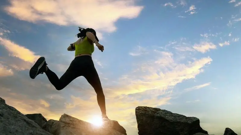 A woman runs and jumps on a mountain ridge at sunset as part of her routine to be physically active