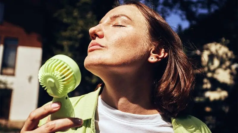 A person using a portable fan in sunny weather.