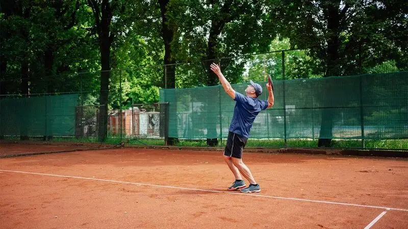 An older adult on a tennis court getting ready to serve and hit the ball