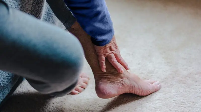 An older adult holds their ankle due to arthritic joint pain
