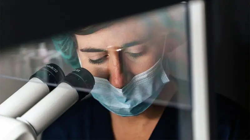 A healthcare professional looking down a microscope.